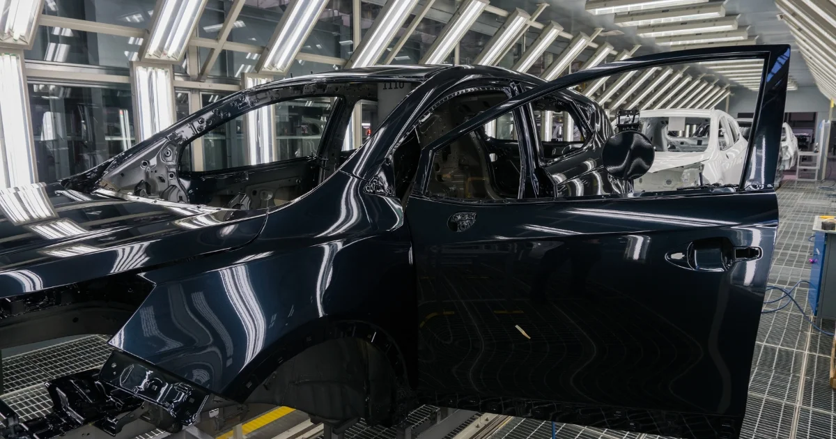 Automotive assembly line with black car bodies under inspection lights.