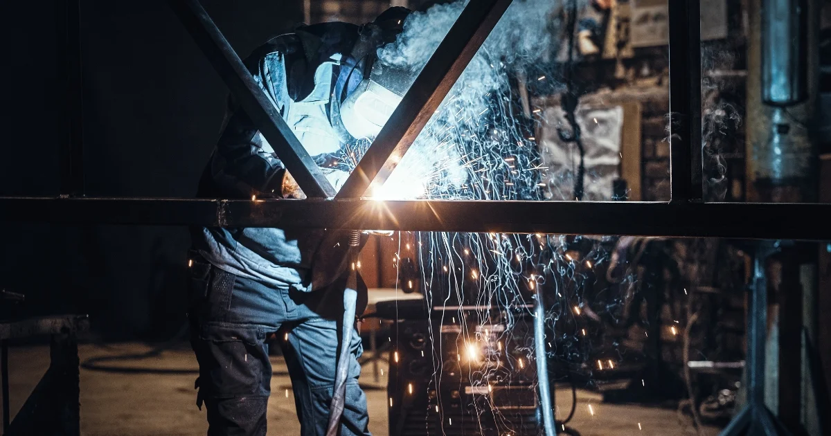 Welder working on a metal frame, sparks flying in a dimly lit workshop