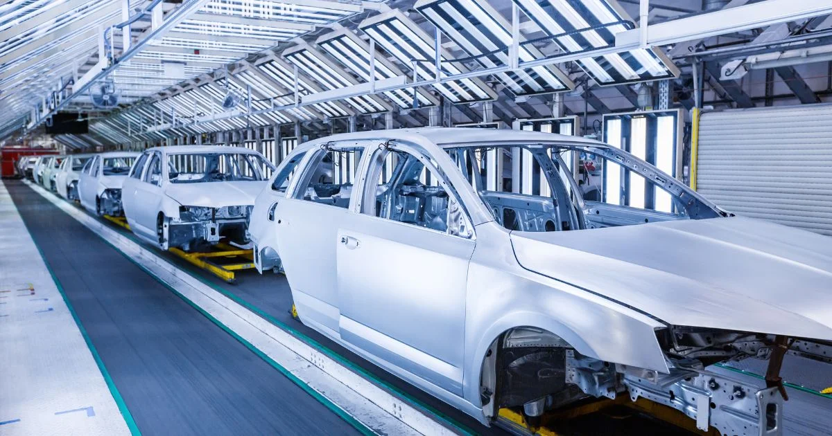 Row of unfinished car bodies moving through a factory drying section.