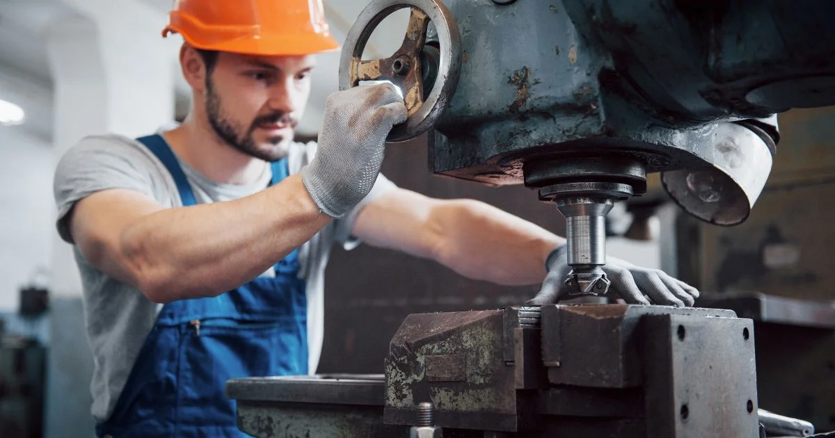 Metalworker operating heavy-duty drill press in industrial workshop.