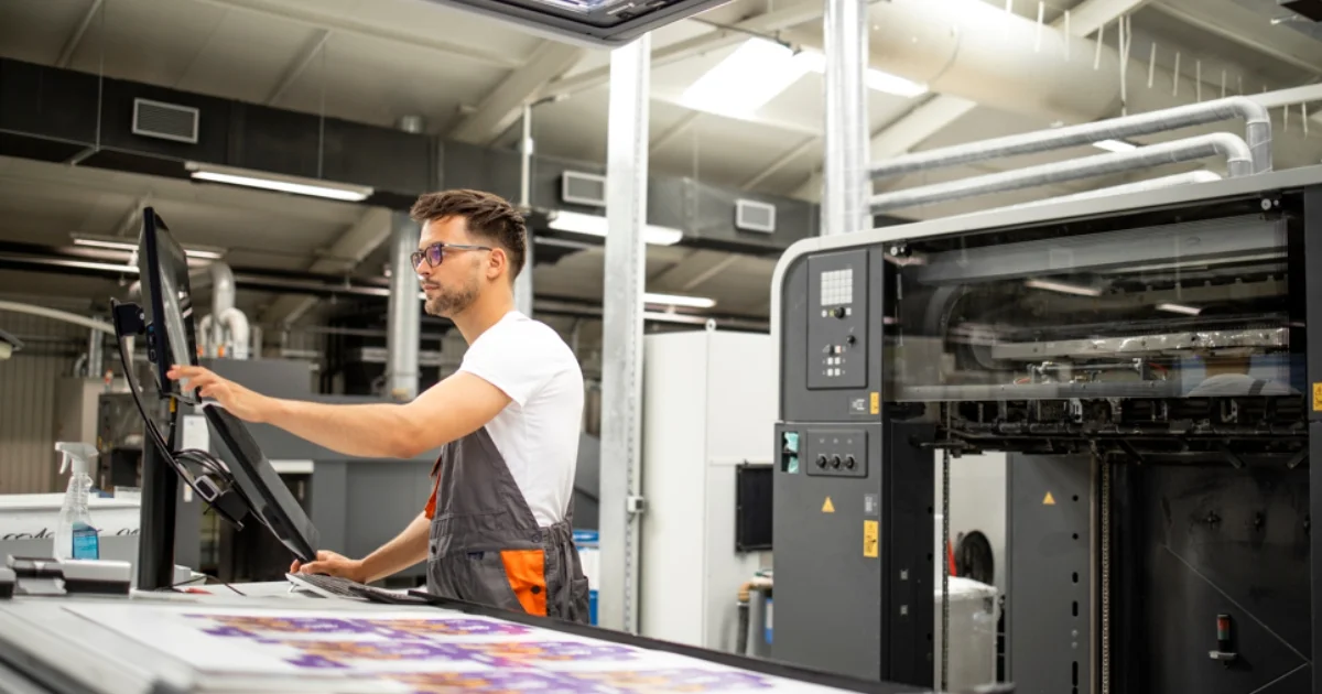 Male printing technician monitoring print quality at a digital printing machine station.