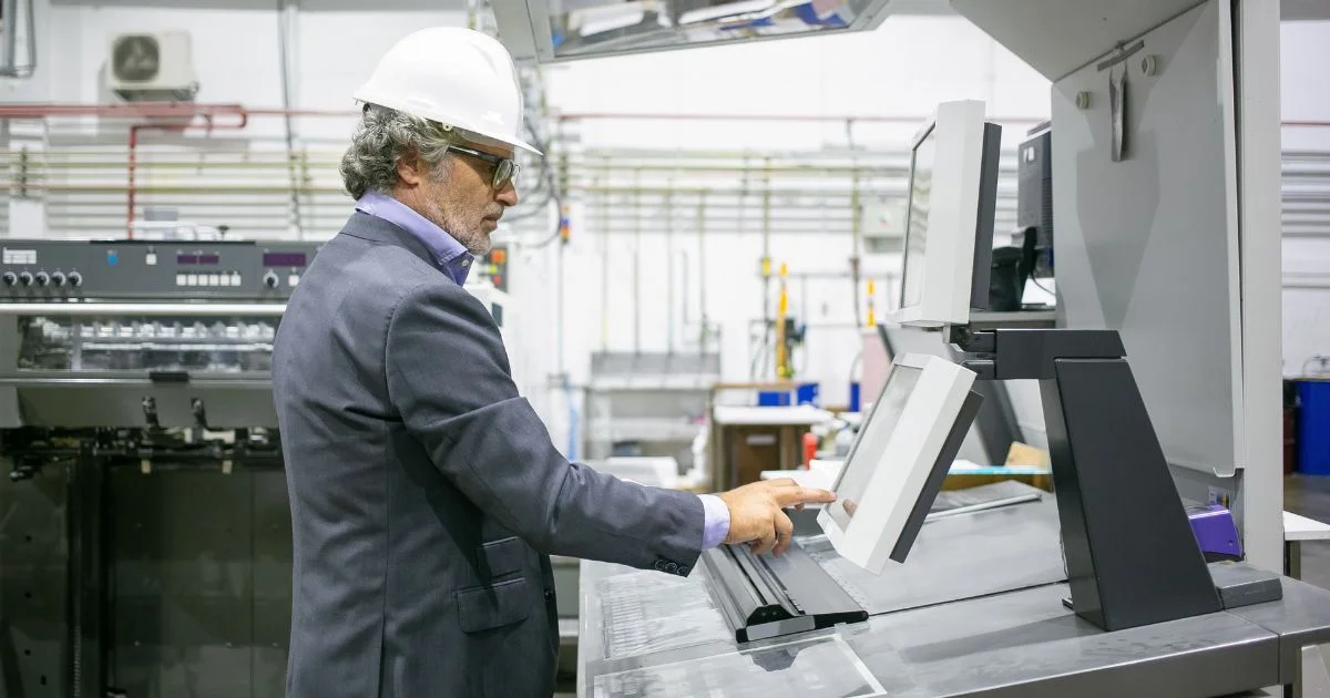 Male factory supervisor in a hard hat operating an industrial control panel in a manufacturing facility.