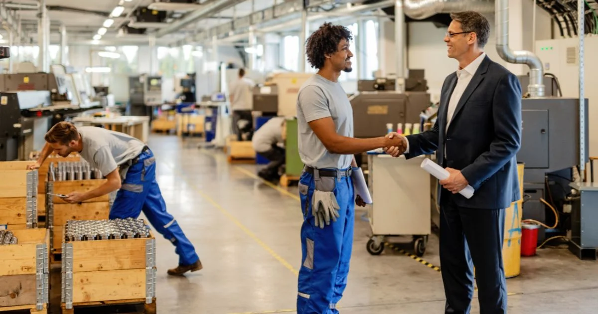 Factory manager and worker shaking hands on manufacturing floor